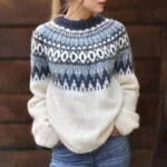 On voit une femme blonde, porté par un pull norvégien blanc et bleu.
