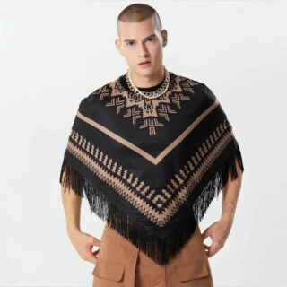 Photo d'un homme debout portant un pull poncho court à col rond ras de cou beige et noir à petites franges fines et motifs géométriques sur un pantalon large marron le tout sur fond gris clair
