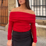 Femme portant un pull épaules dénudées rouge et se trouvant dans la rue.