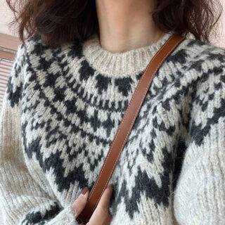 On voit une femme brune qui porte un pull en tricot norvégien