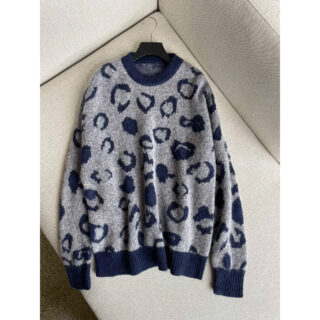 Photo d'un pull léopard bleu marine et gris sur un cintre noir posé sur un sofa gris clair