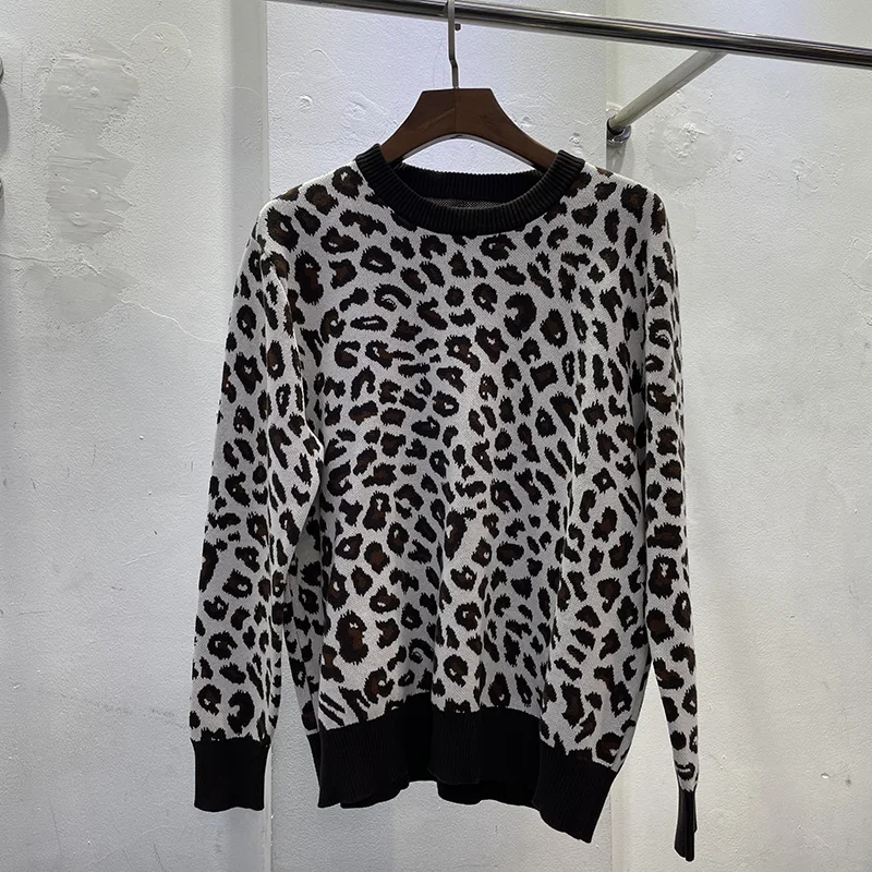 10544-ud3xja.jpg Photo d'un pull léopard fond blanc et impression léopard marron et noire sur un cintre en bois foncé accroché à une tringle en fer sur fond de mur en béton