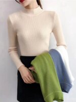 Femme portant un pull col cheminée fin côtelé beige avec des pulls de différentes couleurs sur le bras.