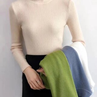 Femme portant un pull col cheminée fin côtelé beige avec des pulls de différentes couleurs sur le bras.