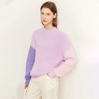 Pull col cheminé tricolore rétro-moderne en trois teinte de mauve, porté par une femme avec un pantalon blanc cassé, une main dans une poche.