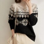 Pull jaquard noir et beige avec des flocons de neige porté par une femme en pantalon beige