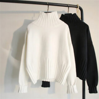Pull col cheminé ample élastique, un blanc et un noir accroché sur un portant.