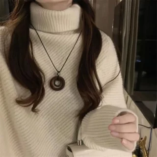 Pull beige à cole roulé porté par une femme portant un collier