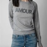 Photo d'une femme portant un pull amour léger en laine et cachemire gris avec des lettres en strass et un jean.