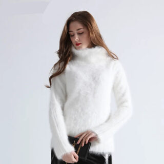 Photo d'une femme debout portant un pull pilou pilou blanc à col cheminée sur un bas noir le tout sur un fond bleu pale