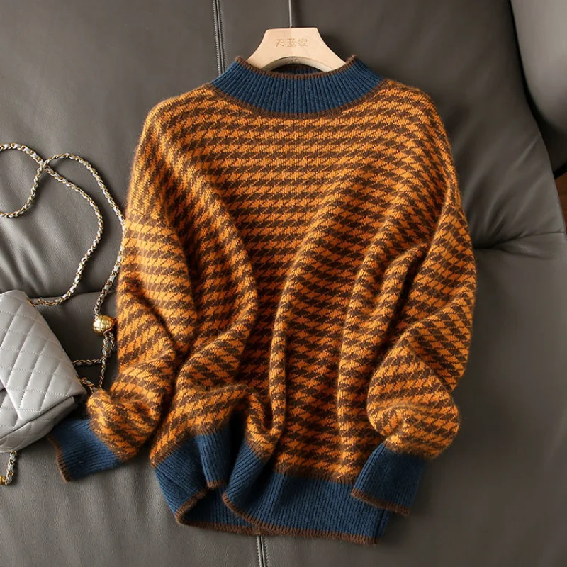 12675-icnlv1.jpg Photo d'un pull vintage pied de poule orange et bleu à col montant et manches longues sur un cintre en bois clair posé sur un divan en cuir gris foncé, un sac gris clair à bandoulière en métal sur la gauche