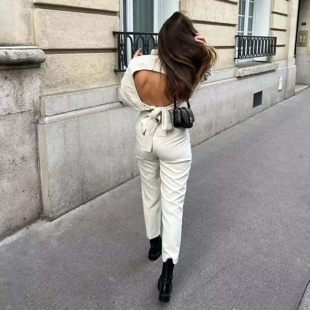 Photo d'une femme portant un pull dos nu en maille texturée beige avec un jean blanc, de dos dans la rue.