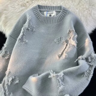 Photo d'un pull gris rock and roll déchiré en forme de croix à col rond sur un fond noir et tapis blanc à poils longs
