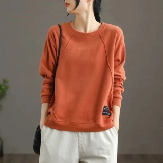 Femme portant un pull orange sur fond gris.