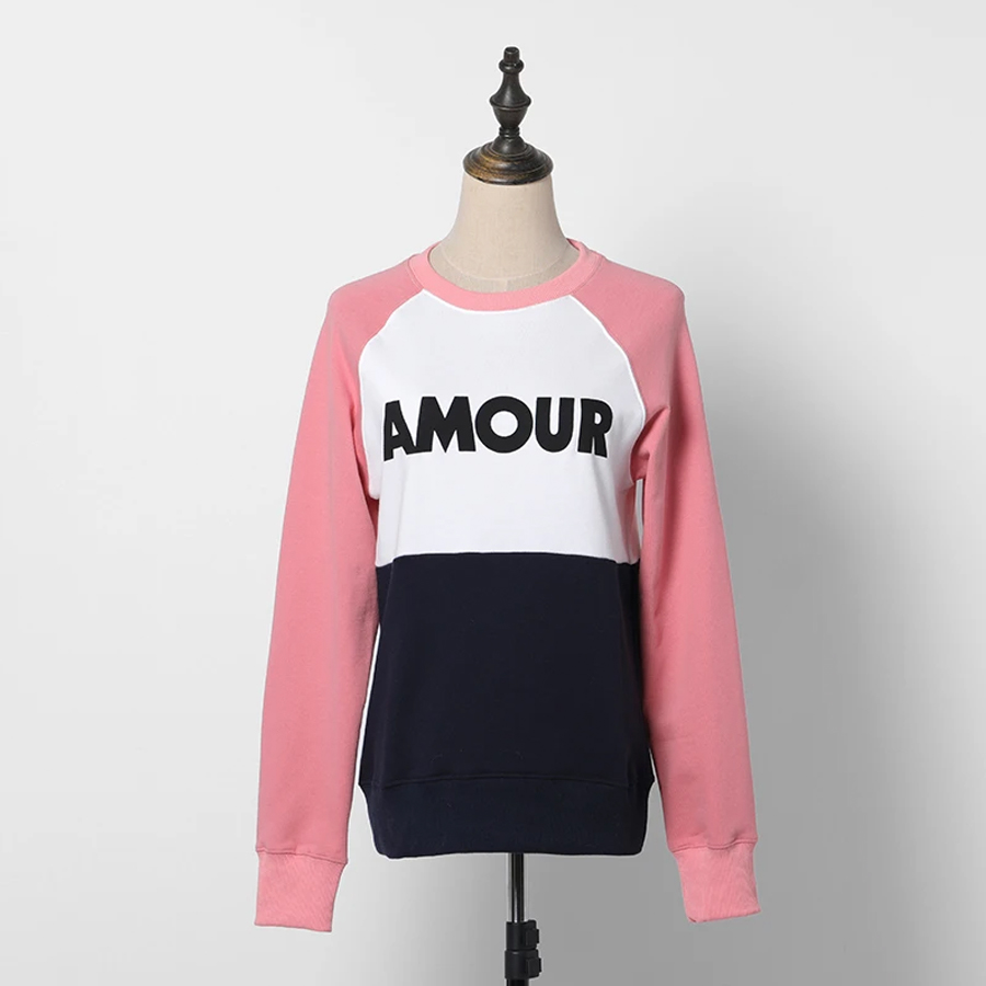 Pull amour pour femme tricolore : les manches roses, le bas bleu foncé et le haut blanc avec l'inscription "AMOUR" en bleu marine. Le pull est sur un mannequin sans tête devant un mur blanc.
