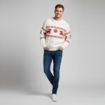 Jeune homme portant un pull de Noël chaud au style scandinave chic blanc avec motif tricoté rouge sur fond gris clair.